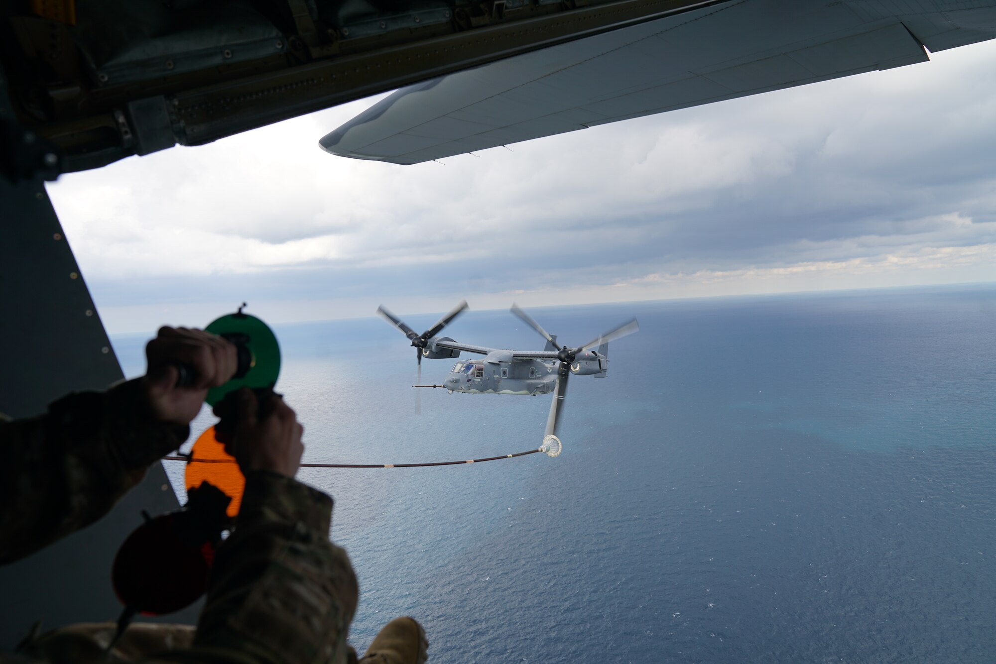 A MC-130J loadmaster signals a CV-22 to begin refueling.