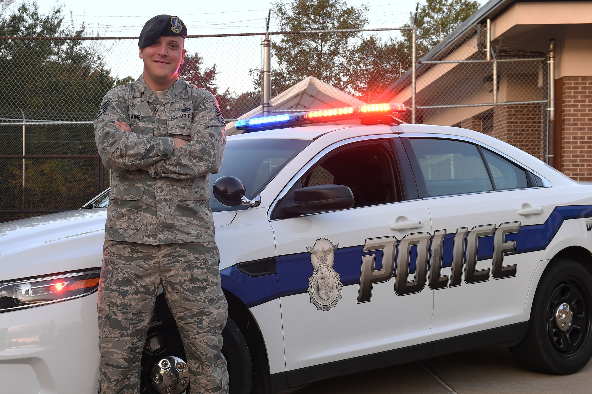 Man stands with crossed arms in front of a police car.