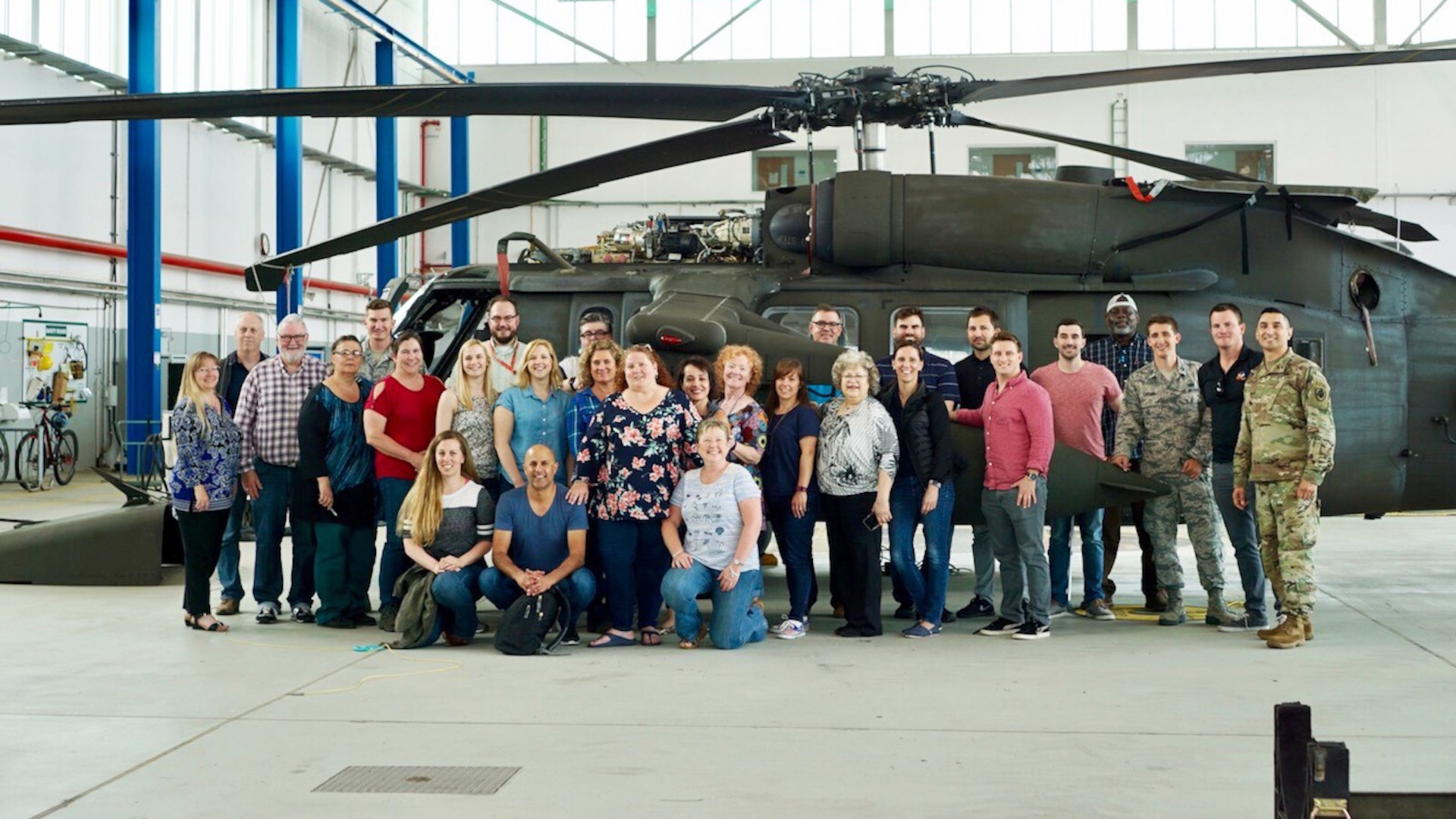 Group of people stand in front of helicopter inside hangar.