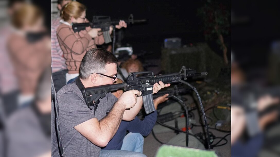 Man points rifle towards targets in an indoor shooting range.