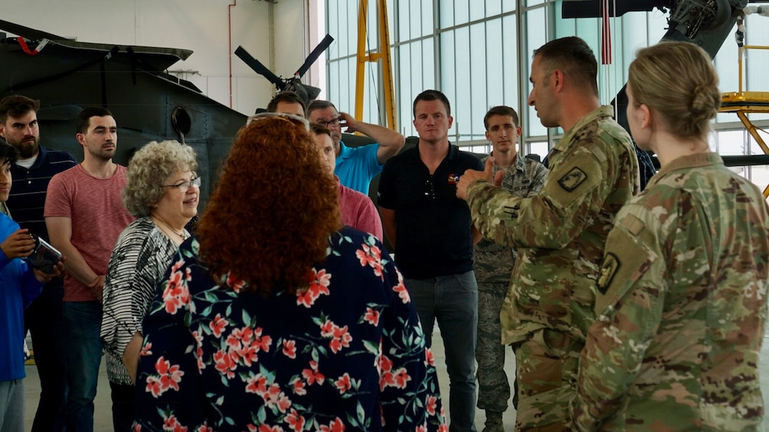 Military and civilian personnel stand in small group listening to a soldier speak.