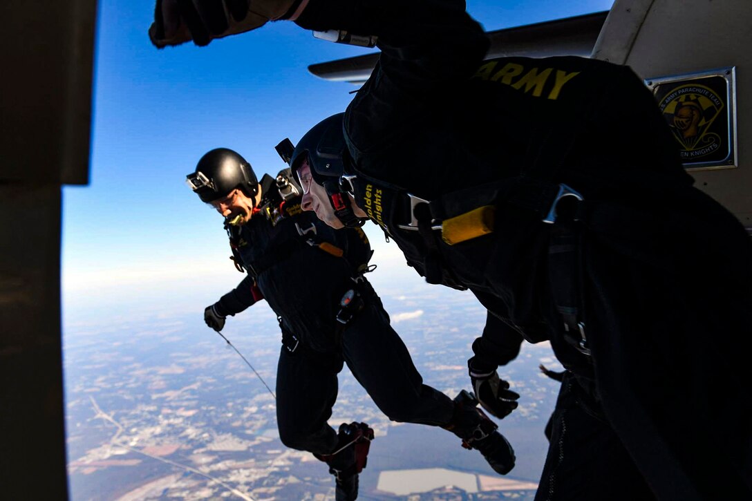 A parachutist suspended just outside an in-flight aircraft looks down at the land below before his parachute deploys.