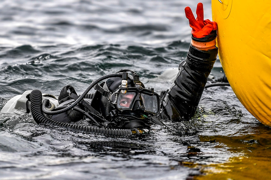 A diver holds up two fingers while submerged in water.