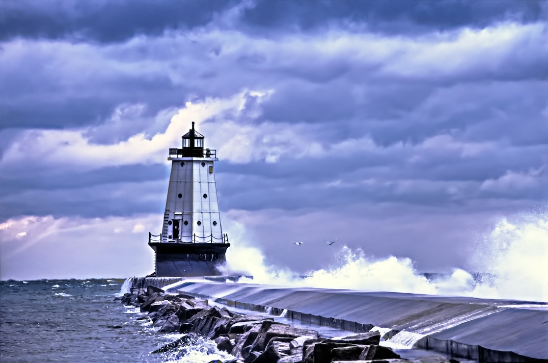 Ludington Lighthouse with waves crashing over the break wall and storm clouds rolling overhead. Ludington, Michigan.