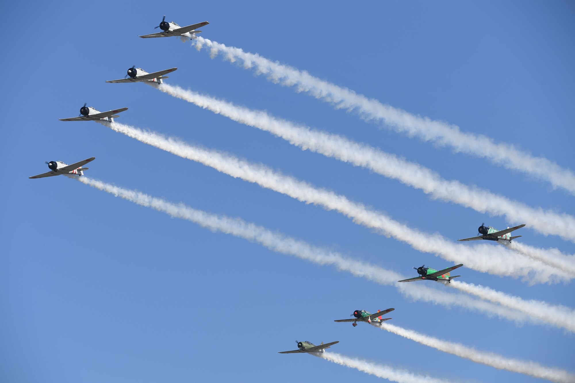 eight Japanese zeros fly in formation from right to left with blue sky behind them