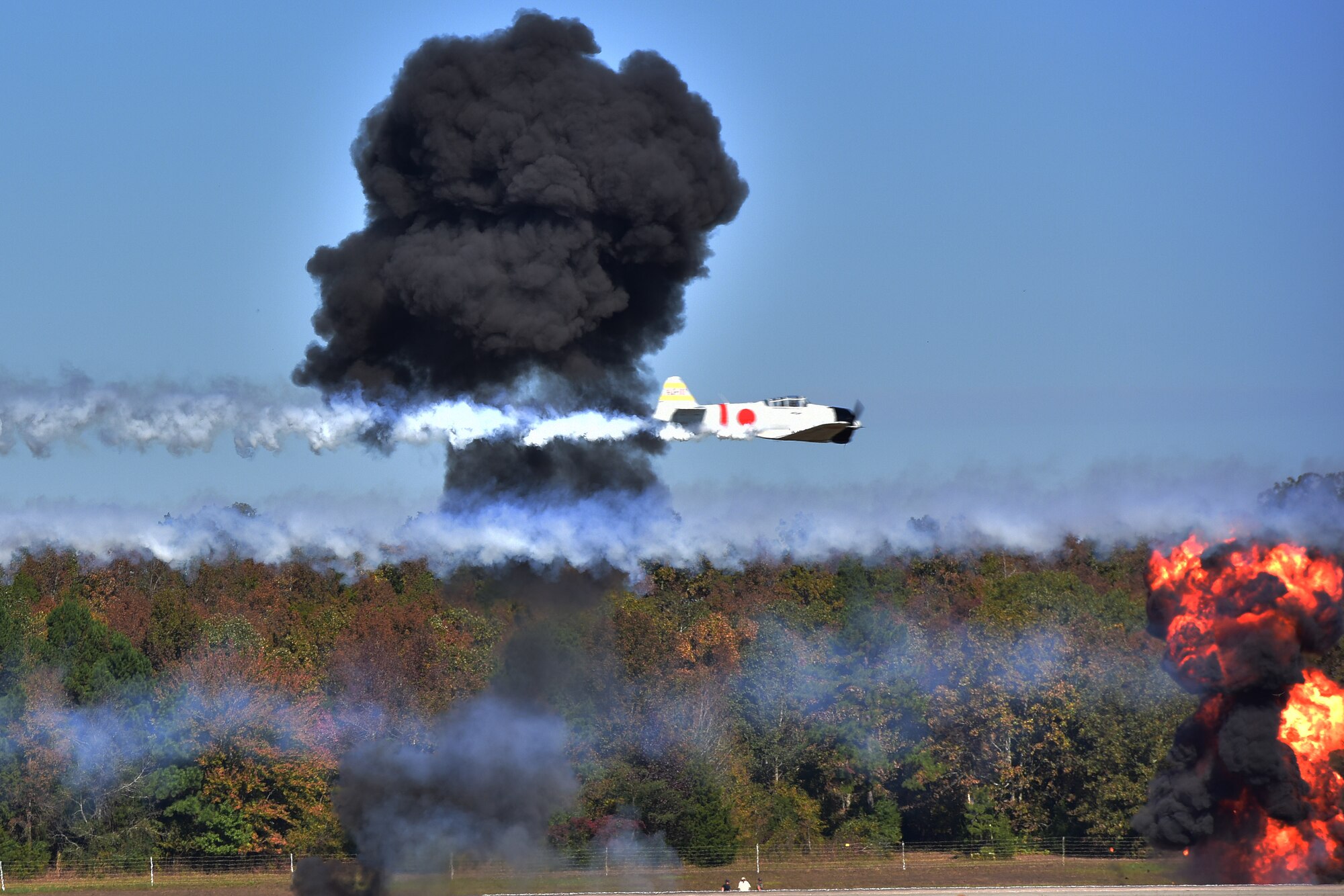 Japanese Zero aircraft fly's over mock explosions simulating attack runs from left to right.