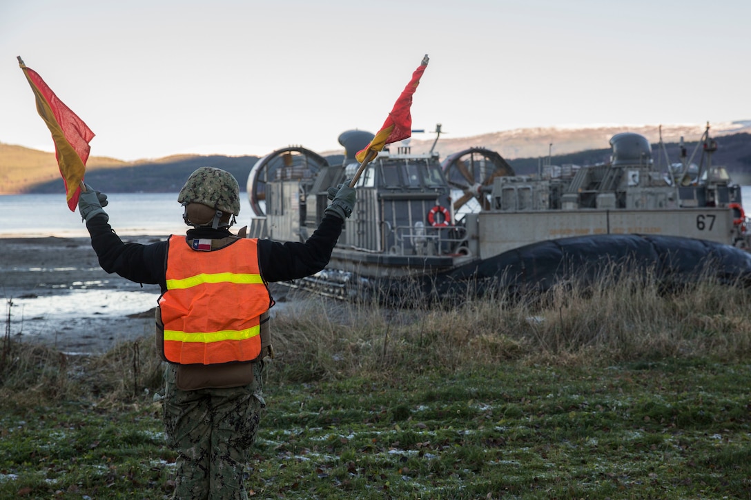 A beach master directs a landing craft air cushion during an amphibious landing in support of Trident Juncture 18 on Alvund Beach, Norway, Oct. 29, 2018. Trident Juncture provides a unique environment for the Marines and Sailors to rehearse their amphibious capabilities. The LCACs originated from USS Iwo Jima (LHD 7) and showcased the ability of the Iwo Jima Amphibious Ready Group and the 24th Marine Expeditionary Unit to rapidly project combat power ashore. (U.S. Marine Corps photo by Lance Cpl. Margaret Gale)