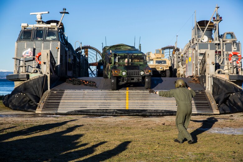 A Marine guides vehicles off of a landing craft air cushion during an amphibious landing in support of Trident Juncture 18 on Alvund Beach, Norway, Oct. 29, 2018. Trident Juncture provides a unique environment for the Marines and Sailors to rehearse their amphibious capabilities. The LCACs originated from USS Iwo Jima (LHD 7) and showcased the ability of the Iwo Jima Amphibious Ready Group and the 24th Marine Expeditionary Unit to rapidly project combat power ashore. (U.S. Marine Corps photo by Lance Cpl. Margaret Gale)