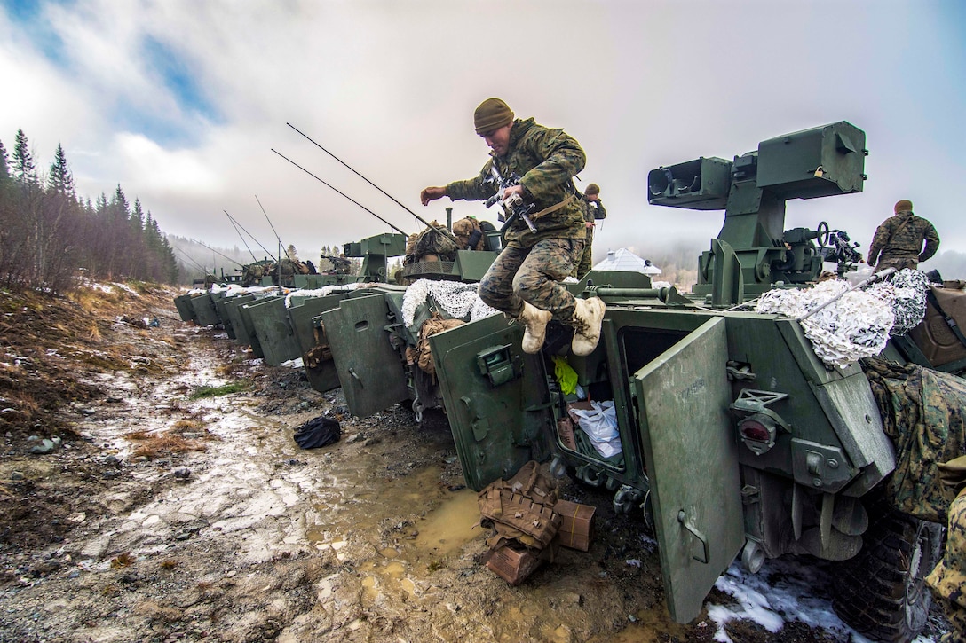 A Marine jumps from the top of a military vehicle