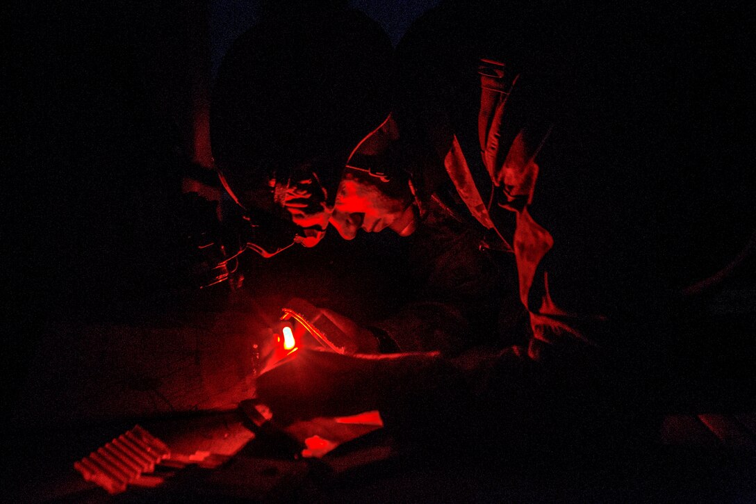 A Marine leans over planning materials in darkness, illuminated by red light.