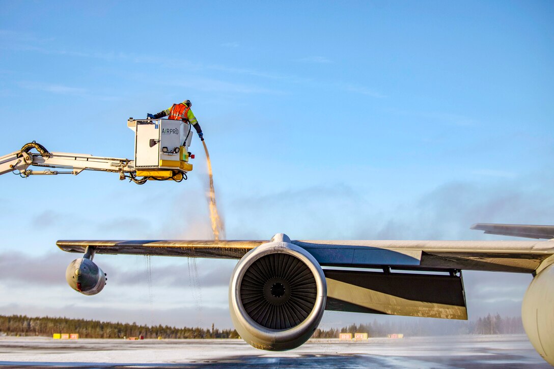 A worker in a raised container sprays an aircraft wing to de-ice it.