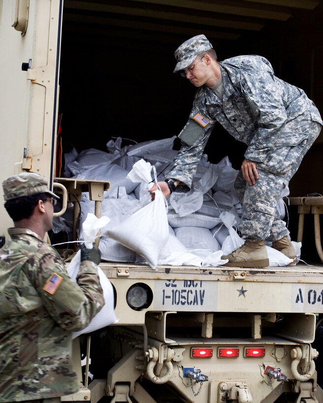 Soldiers load sandbags onto a tactical vehicle.