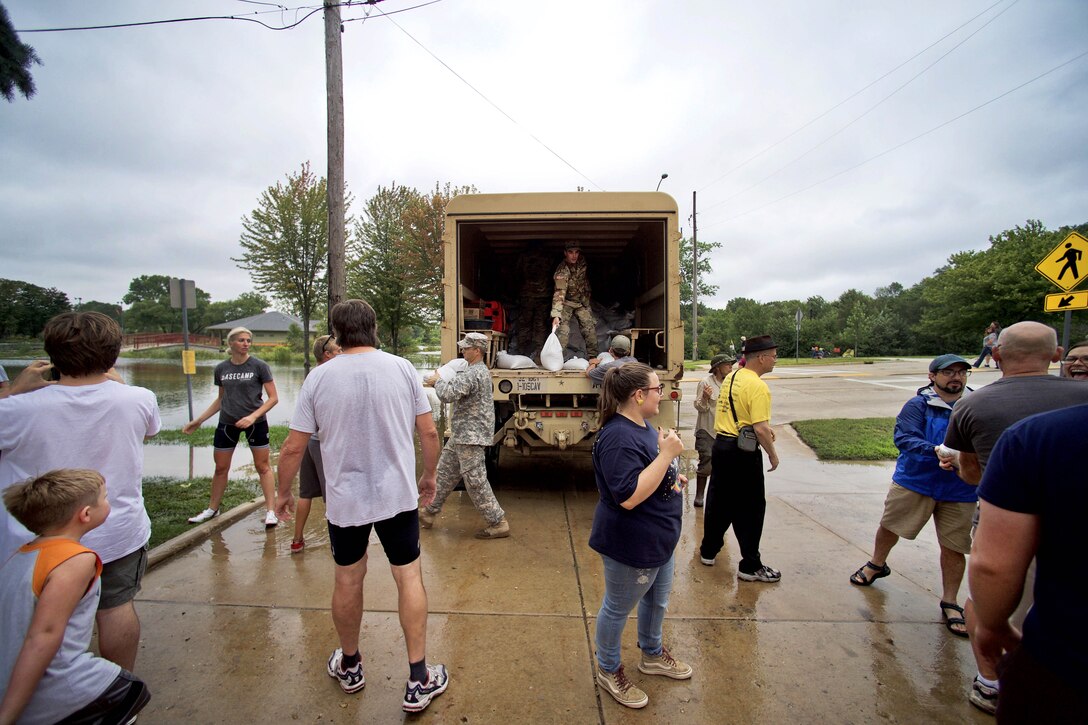 People carry sandbags from a military vehicle.