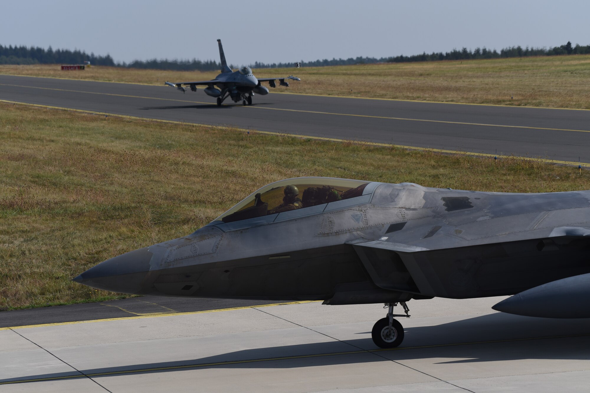 A U.S. Air Force F-22 Raptor from the 95th Fighter Squadron, 325th Fighter Wing, at Tyndall Air Force Base, Fla., and a U.S. Air Force F-16 Fighting Falcon assigned to the 480th Fighter Squadron, Spangdahlem Air Base, Germany, taxis down the flightline at Spangdahlem AB, Aug. 29, 2018. The aircraft trained with other NATO partners during the F-22 Flying Training Deployment. (U.S. Air Force photo by Airman 1st Class Branden Rae)