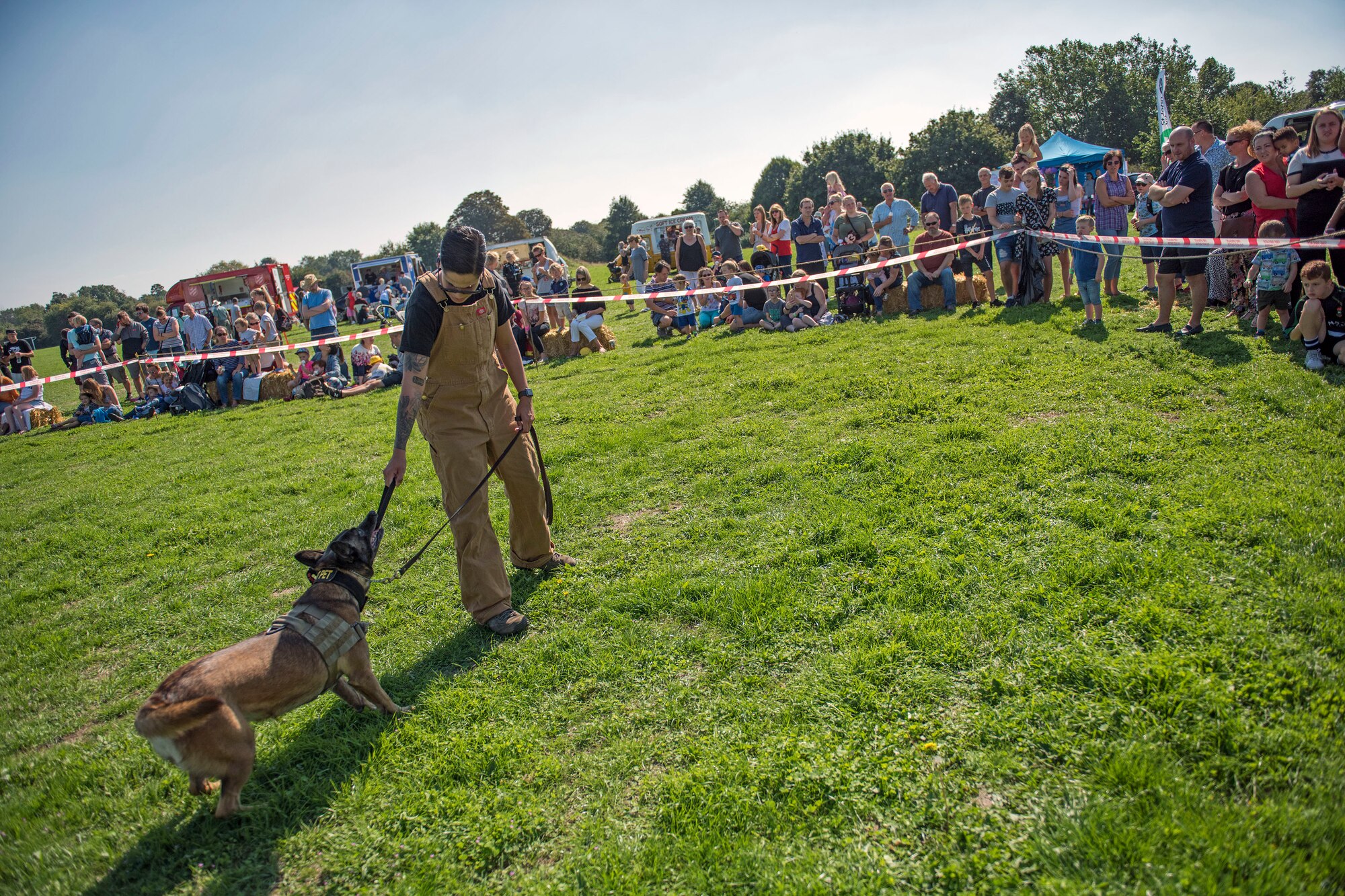 U.S. Air Force Staff Sgt. Kristina Santos, 100th Security Forces Squadron military working dog handler and MWD Yuki, play in front of a crowd at the Newmarket Fire and Police Fun Day in Newmarket, England, Sept. 2, 2018. The MWD’s and handlers demonstrated chest and back bites as well as the “six-phases of aggression.” (U.S. Air Force photo by Staff Sgt. Christine Groening)