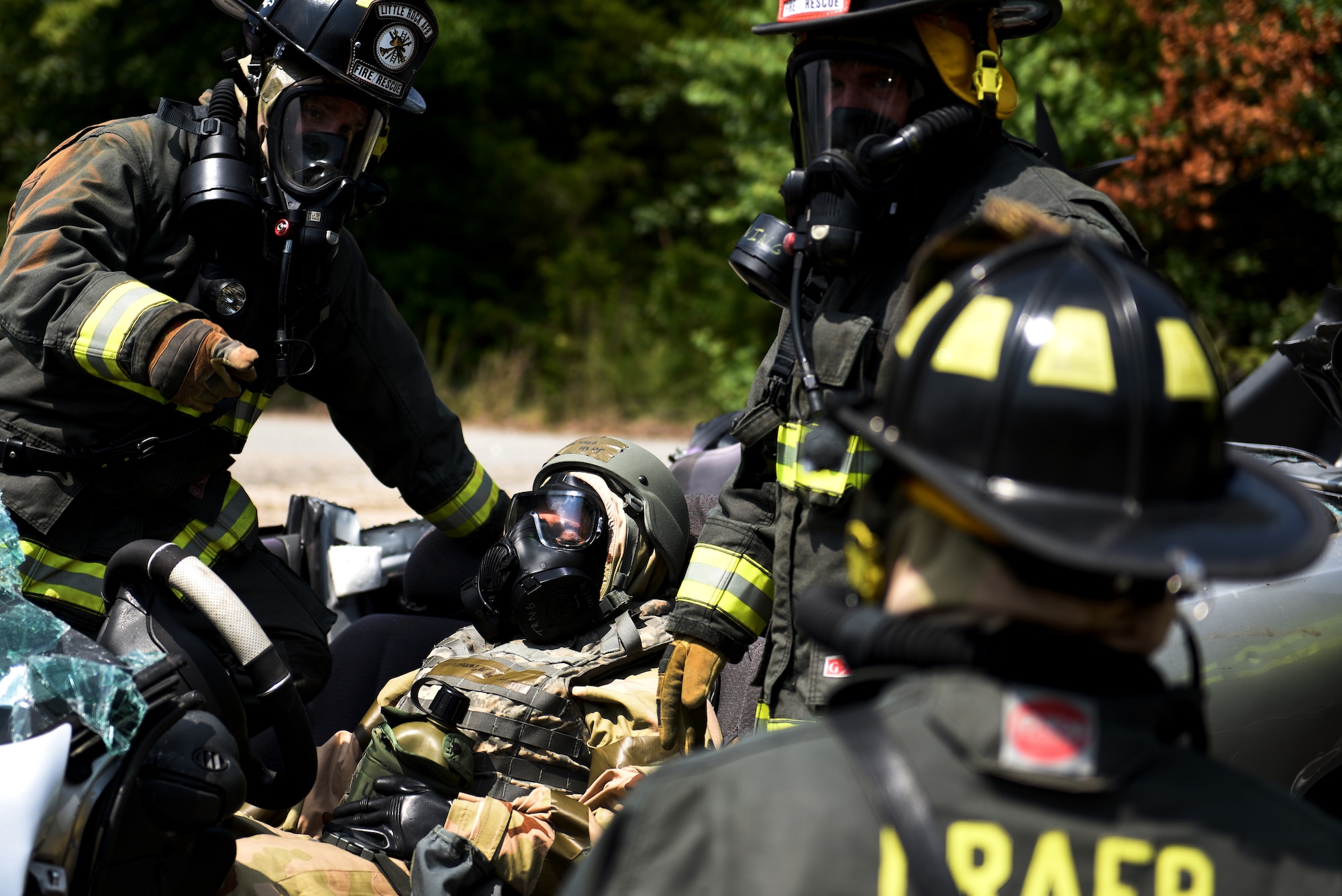 Firefighters in MOPP gear practice rescuing an Airman in MOPP gear from a car crash.