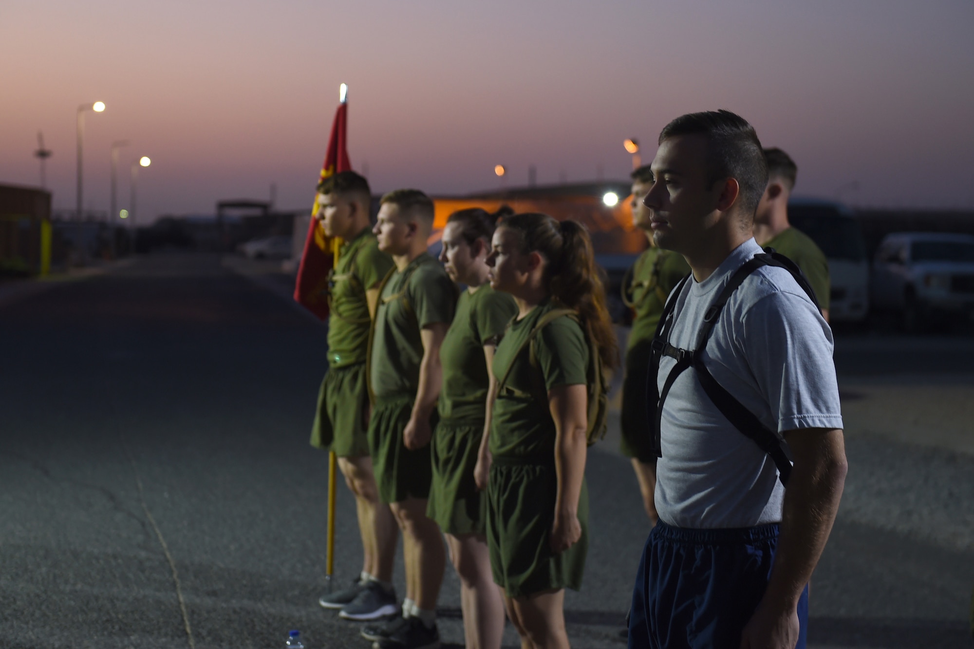 An Airman stands in formation with Marines as the sun rises