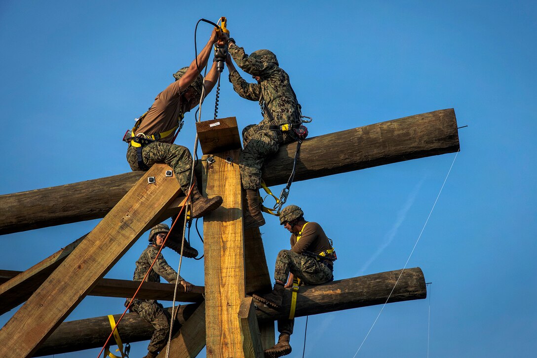 Sailors use a hydraulic drill to secure beams while building a 30-foot watch tower.