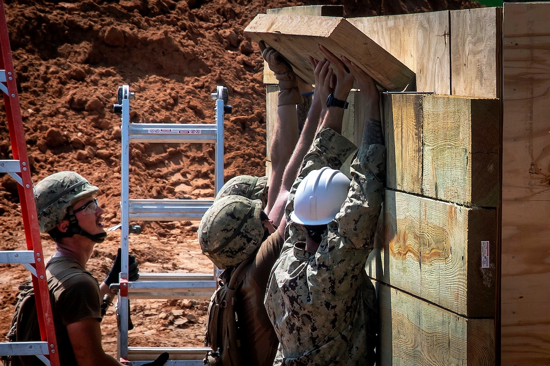 Sailors secure beams while building a bunker during a field training exercise.