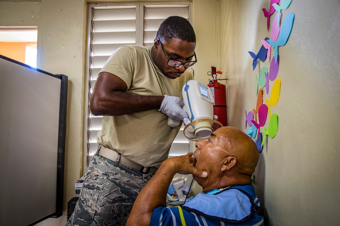 An airman aims an x-ray machine at a patient.