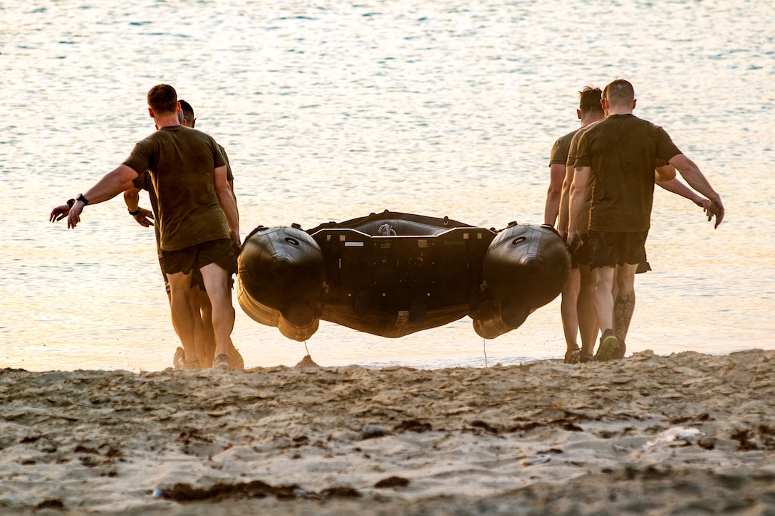 Soldiers carry an inflatable boat on a beach.
