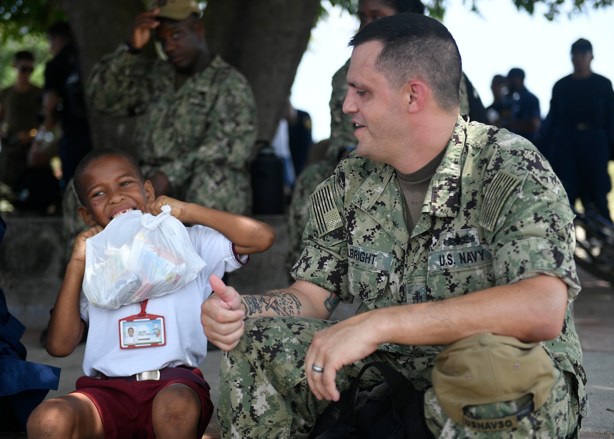 A U.S. Navy Sailor  helps a student at Gimnasio Cristiano de Bocachica children’s school open his lunch bag.