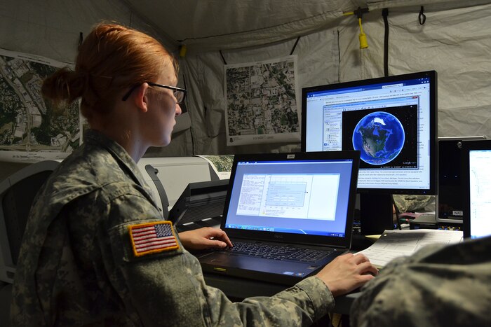 A soldier looks at images of the Earth on computer monitors.