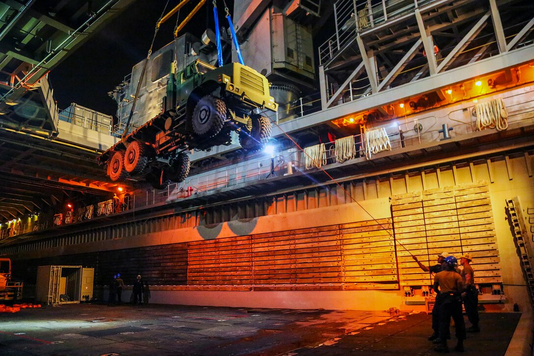 Sailors hoist a vehicle.