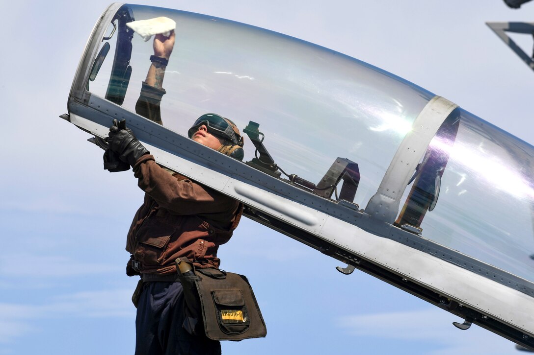 A sailor cleans the glass of a plane's cockpit.