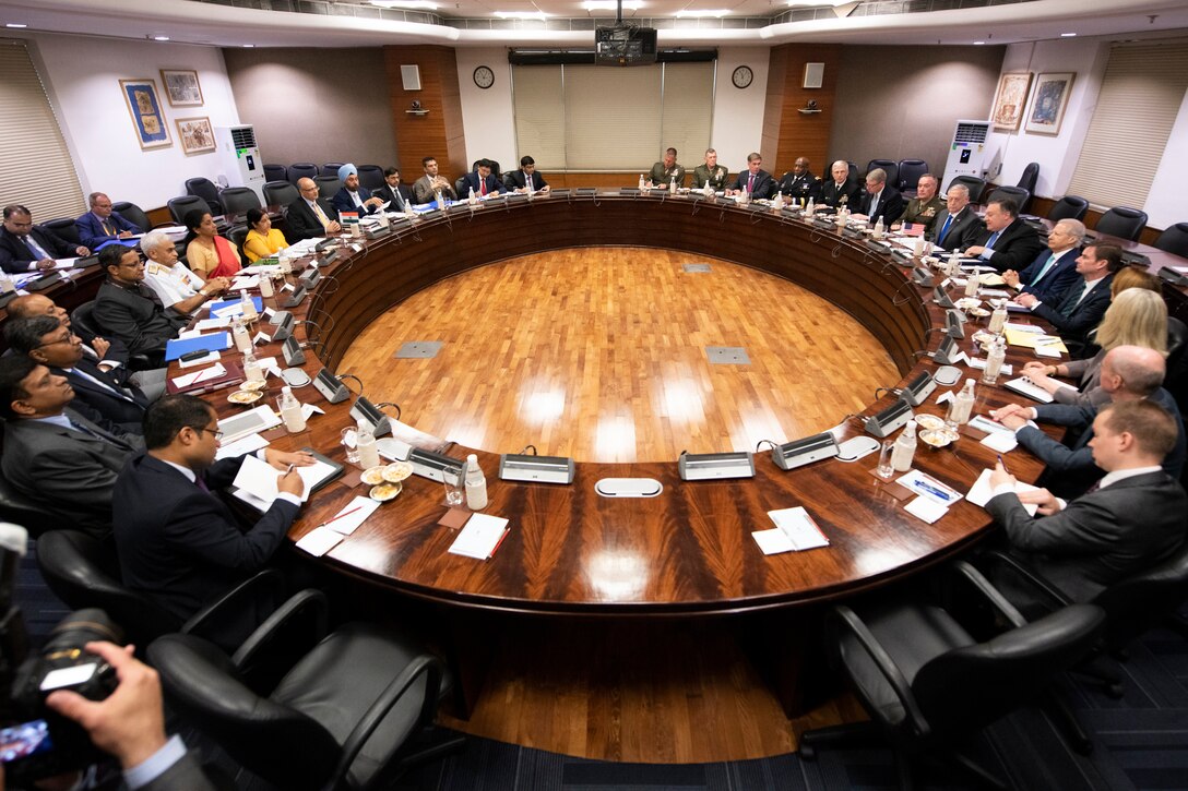Top U.S. and Indian defense officials sit around an oval table for a meeting.
