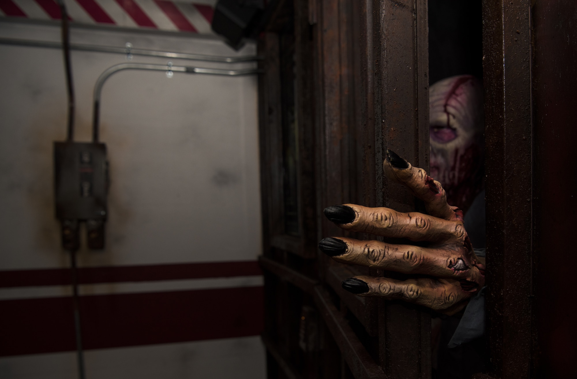A zombie peaks through the crack of a door during a Mobile Escape Room session on Joint Base McGuire-Dix-Lakehurst, N.J., Aug. 27, 2018. The “zombie” added pressure to the timed game of a players working together to solve individual puzzles and riddles in order to escape. (U.S. Air Force photo by Airman Ariel Owings)