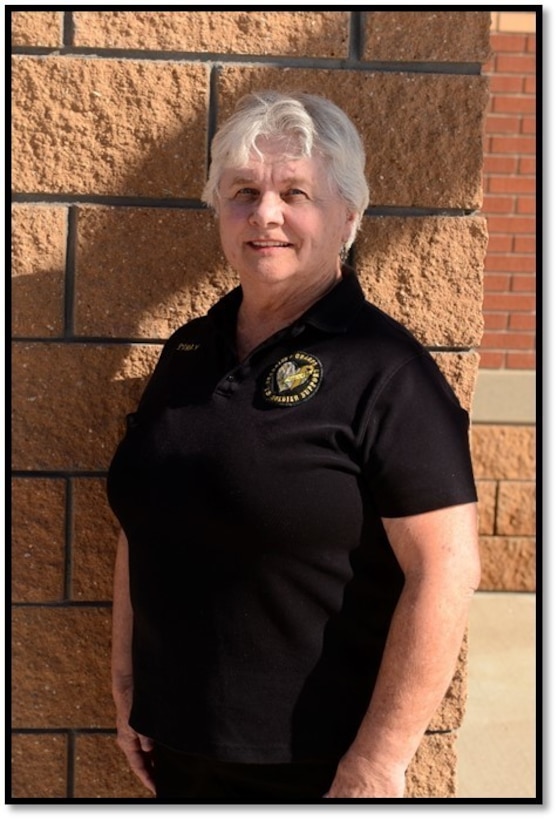 A woman poses against a brick wall while wearing a black polo shirt.