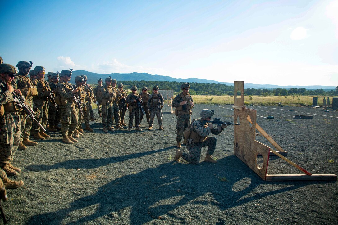 Marines receive a demonstration on engaging targets from behind a wooden structure.