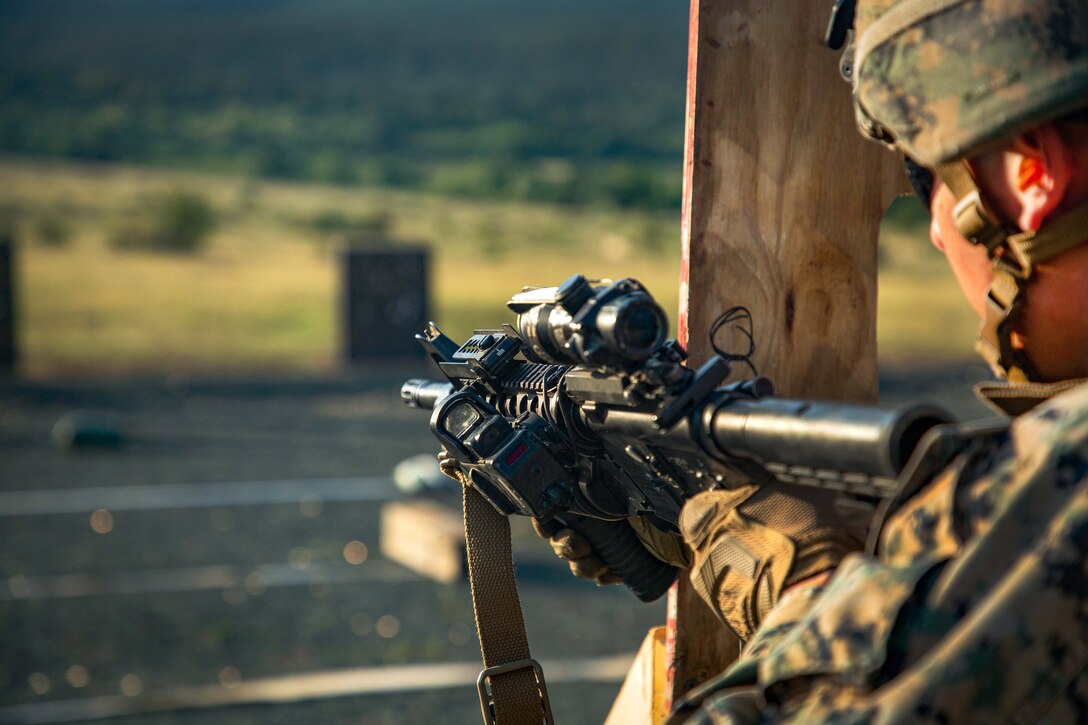 A Marine reloads his weapon after firing at targets from behind a wooden structure.
