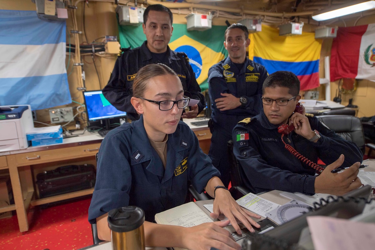 U.S. and multinational Sailors work at desks on USS Gunston Hall.