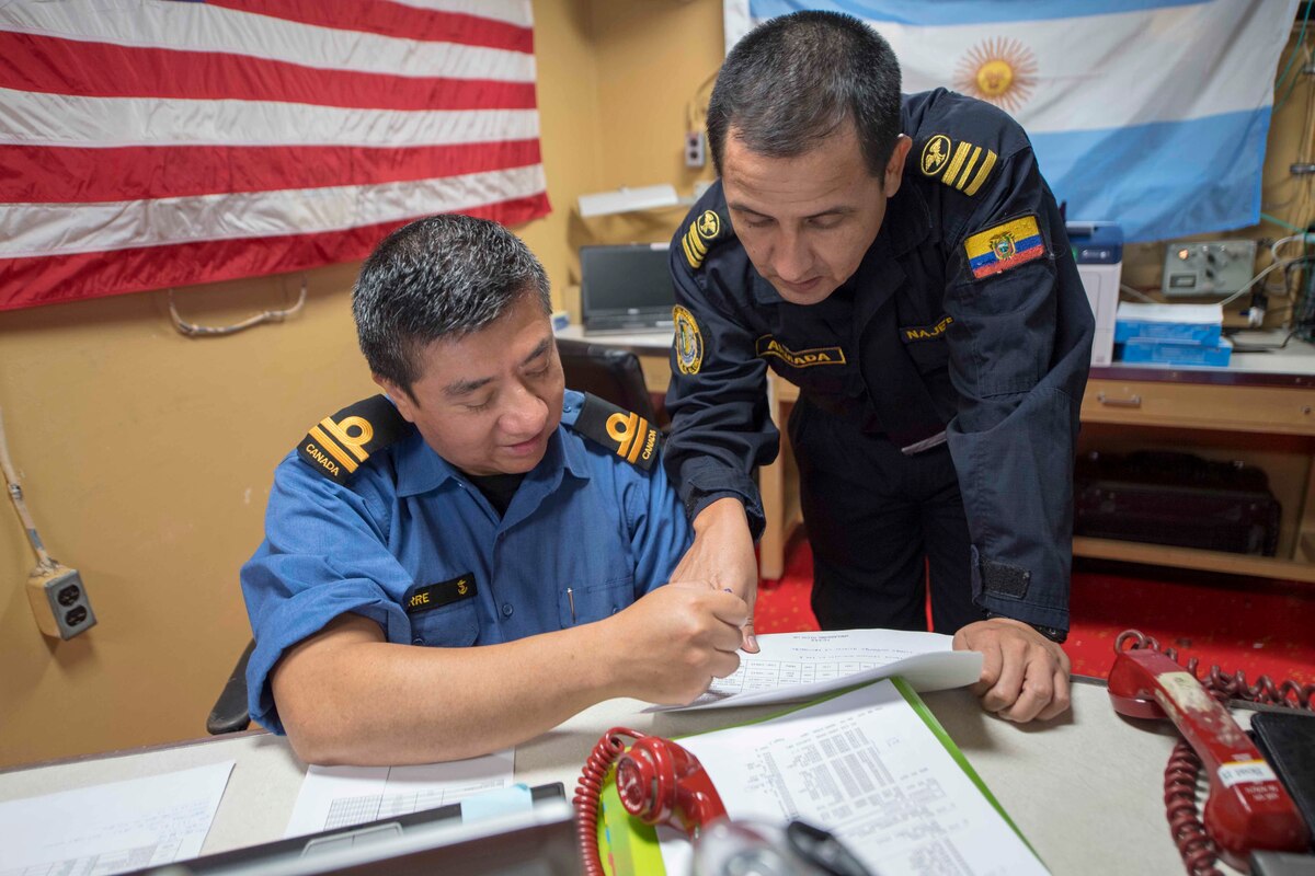 A Royal Canadian Navy officer and an Ecuadorian Navy officer review a schedule of events while aboard USS Gunston Hall.