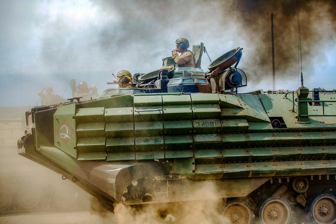 Marines ride a vehicle through dust.