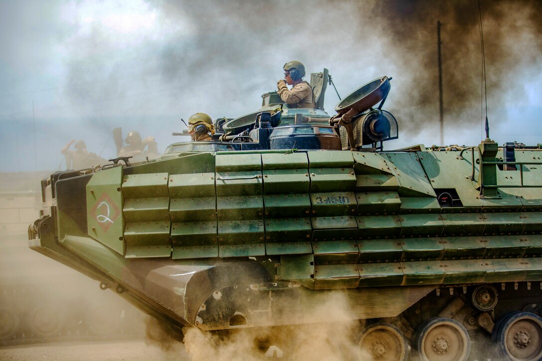 Marines ride a vehicle through dust.