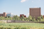 Landscape photo of UMBC sign at entrance to the campus during a sunny day. Three academic buildings are visible behind the sign.