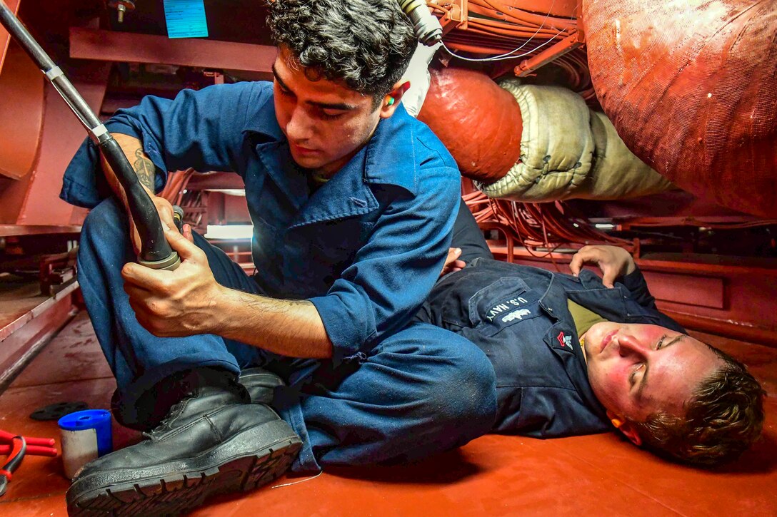 Sailors work on an engine in a tight space.