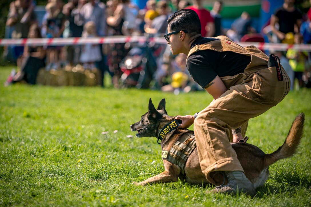 An airman holds the collar of her military working dog in front of an audience.