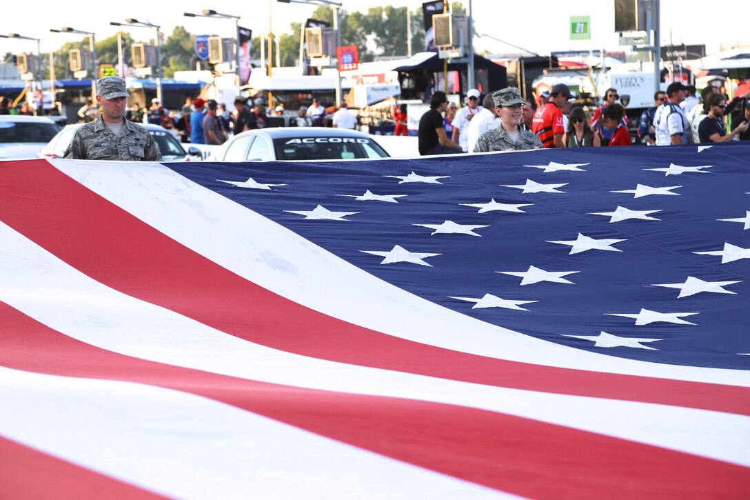 At right, Master Sgt. Karen Ridge, 932nd Aeromedical Evacuation Squadron, smiles as the American flag waves just prior to the national anthem.  As part of the racing event, 932nd Airlift Wing Maintenance Group commander, Col. Sharon Johnson, was recognized on stage with the Indy drivers at the Bommarito Automotive Group 500 Aug. 25, 2018, Gateway Motorsports Park, Madison, Illinois. Johnson was an honored VIP to help kick off the 2nd annual IndyCar race which was won by Will Power,  won the 248-lap race around the four-turn, 1.25-mile Gateway Motorsports Park oval paved track in Madison, Illinois, in his #12 Chevrolet by 1.3117 seconds over second place finisher Alexander Rossi.  The 932nd Airlift Wing was represented by maintenance, medical, public affairs staff and operations personnel.  (U.S. Air Force photo by Lt. Col. Stan Paregien)