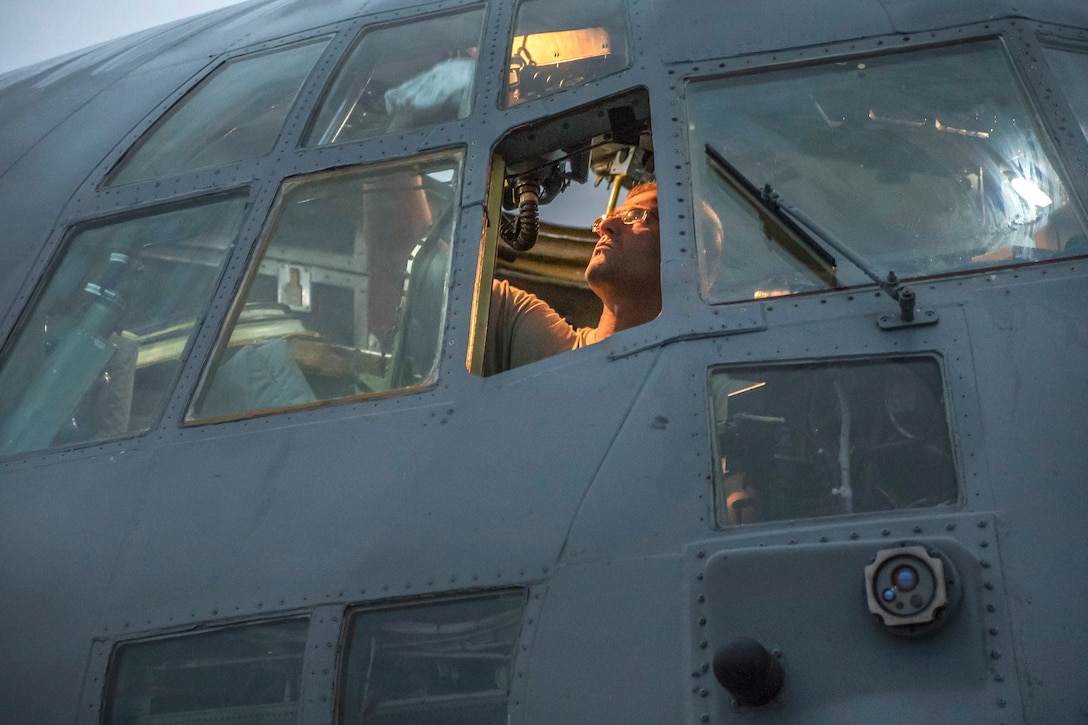 An airman cleans the windows inside the cockpit of an aircraft during routine preflight operation.