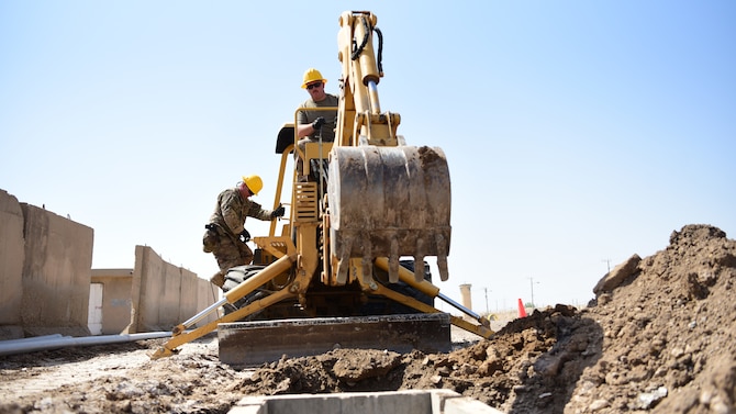 U.S. Air Force Tech. Sgt. Keith Robertson, Air Force Engineering and Installation, Iraq cable and antenna systems specialist, dismounts while Staff Sgt. Allen Cantrell, AF-EI equipment operator, uses a backhoe to dig a trench Aug. 28, 2018, at Camp Taji, Iraq. Robertson and Cantrell are assisting in the completion of a ‘fiber ring,’ which will provide personnel at Camp Taji faster and more secure network connections. (U.S. Air Force photo by Staff Sgt. Christopher Stoltz)