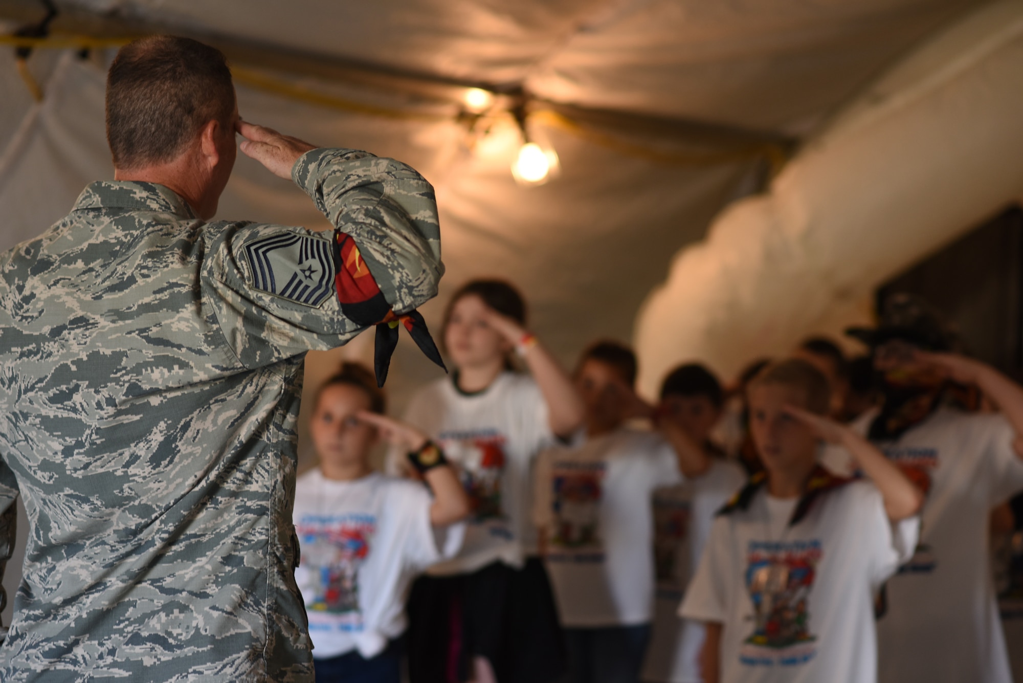 Chief Master Sgt. Richard Beard, 145th Aircraft Maintenance Squadron superintendent, teaches a group of nine to ten year-olds how to salute during the Annual North Carolina (NC) Operation Kids on Guard held at the NC Regional Training Site in Stanly County, Sept. 8, 2018. Children of military members were able to join in activities including short aircraft rides, engaging with military members while learning flight structure and commands, interactive displays with a C-17 Globemaster III and other aircraft, as well as a ropes course and bouncy castles.