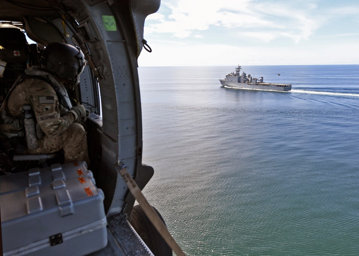 A U.S. Soldier observes USS Gunston Hall from aboard an Army UH-60L helicopter.