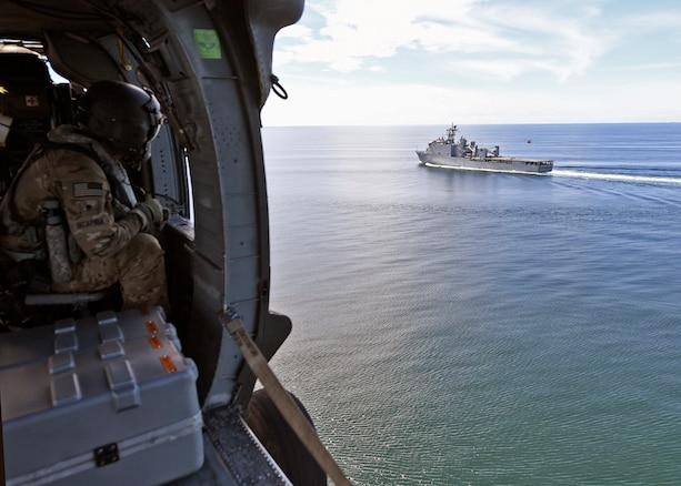 A U.S. Soldier observes USS Gunston Hall from aboard an Army UH-60L helicopter.