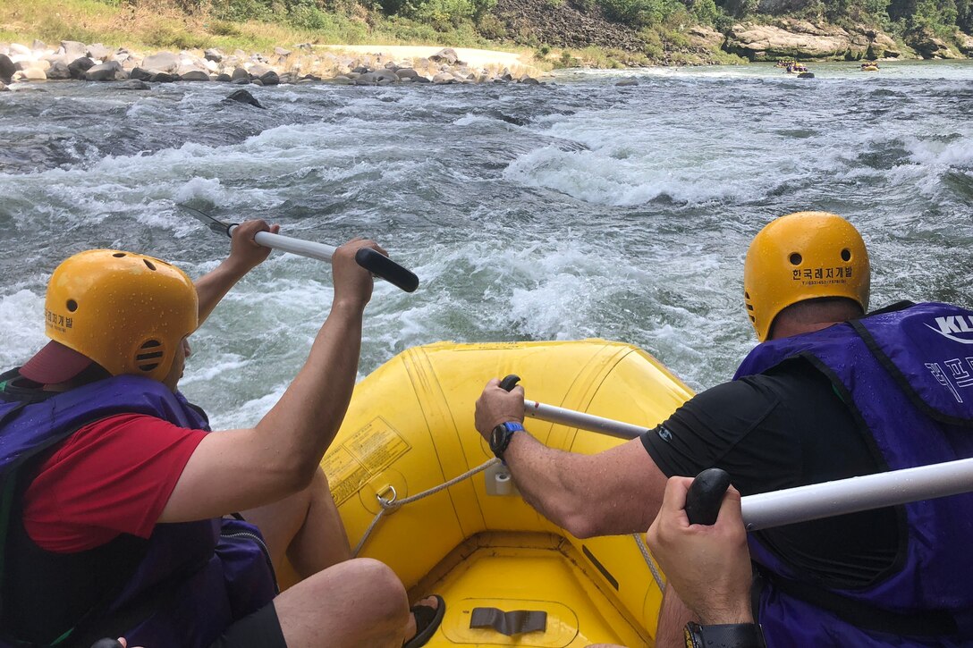 Service members paddle a raft through rapids on a river in South Korea.