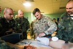 U.S. soldier teaches Bulgarian soldier how to tend a wound.