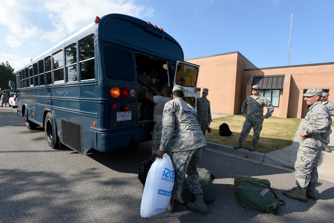 Airmen load bags of ice on the back of a bus.